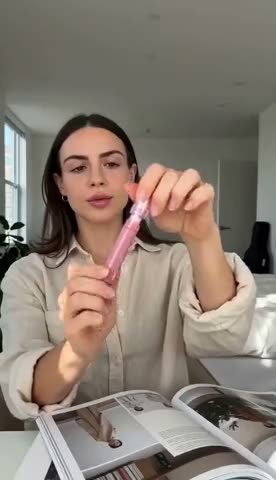 A pink lip stick uncapped and applied at a desk over an open magazine, ending on a close-up of the finished lip.